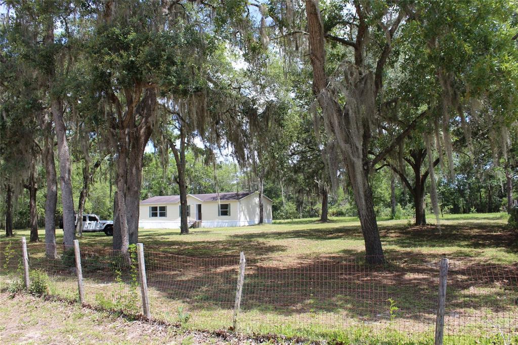 A single-story manufactured home sits on a grassy lot shaded by large, moss-covered oak trees — 112 JUNIPER DRIVE, HAWTHORNE, FL