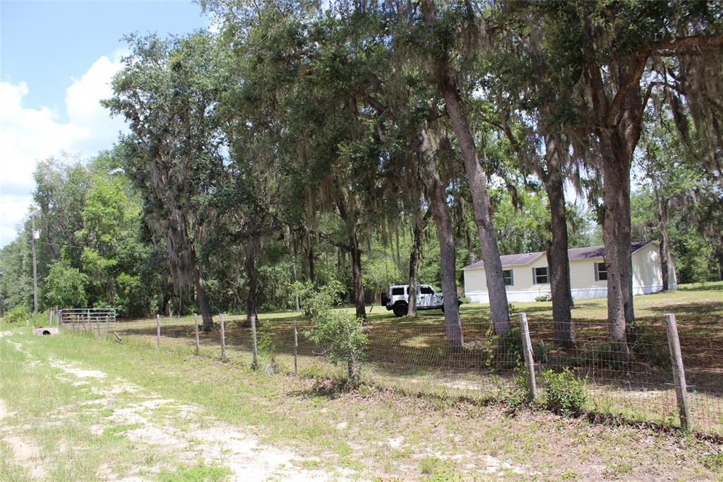 A white mobile home sits behind a wire fence on a wooded lot with trees — 112 JUNIPER DRIVE, HAWTHORNE, FL