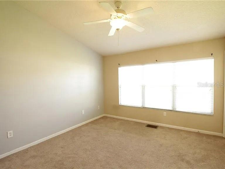 An empty bedroom features beige carpeting, light gray walls, a ceiling fan, and large windows — 4514 BARNSTEAD DRIVE, RIVERVIEW, FL