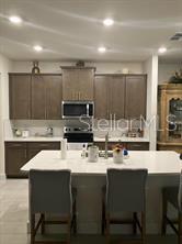 A kitchen features brown cabinets, a white island with bar stools, and stainless steel appliances — 4258 SW SW 53RD LANE, OCALA, FL