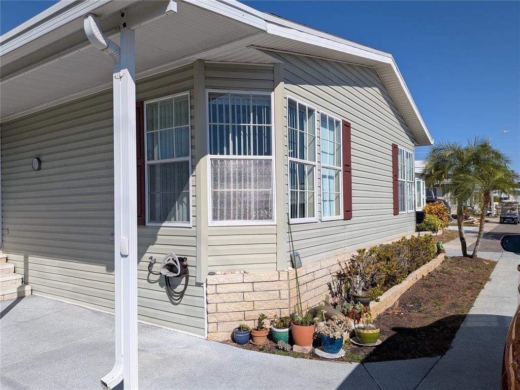 The exterior of a light green manufactured home features a bay window and potted plants — 34709 LAKE DRIVE N, PINELLAS PARK, FL