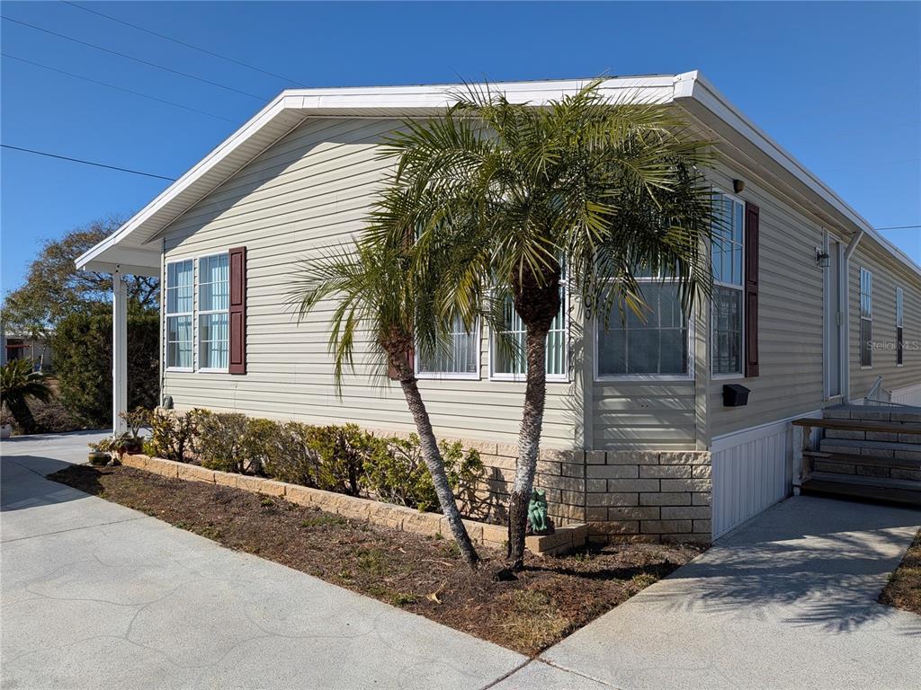 A light-colored mobile home with a palm tree, brick skirting, and a concrete driveway — 34709 LAKE DRIVE N, PINELLAS PARK, FL