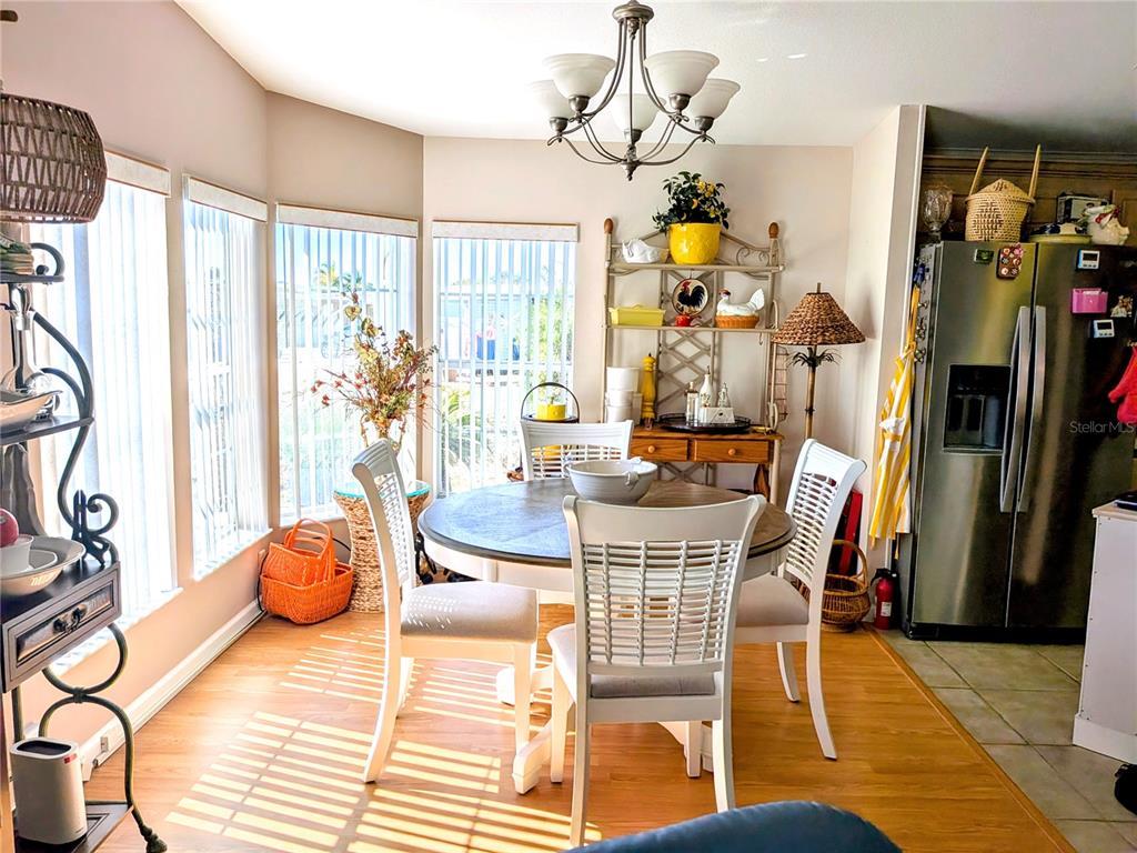 A dining area features a round table, white chairs, a chandelier, and large windows — 34709 LAKE DRIVE N, PINELLAS PARK, FL