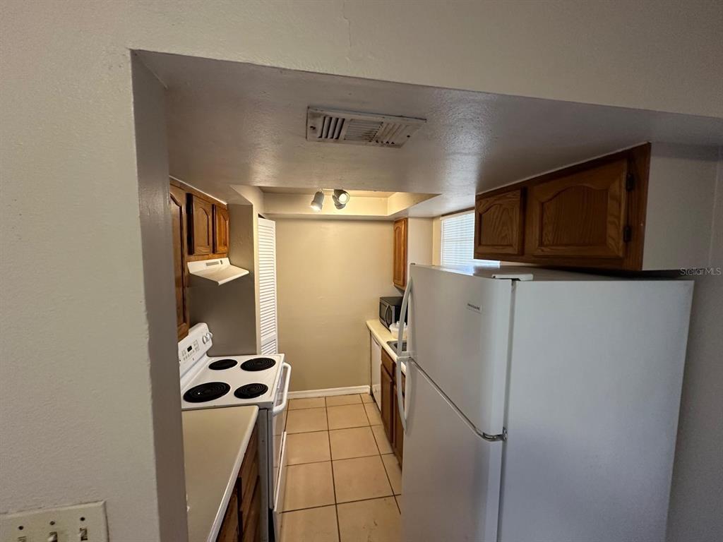 A galley-style kitchen features white appliances, wood cabinets, and light-colored floor tiles — 1300 ARLINGTON LANE NE UNIT 114, PALM BAY, FL