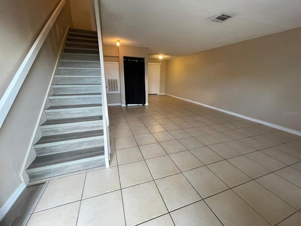 A room with beige tile flooring, a staircase with wood-look treads, and two doorways — 1300 ARLINGTON LANE NE UNIT 114, PALM BAY, FL