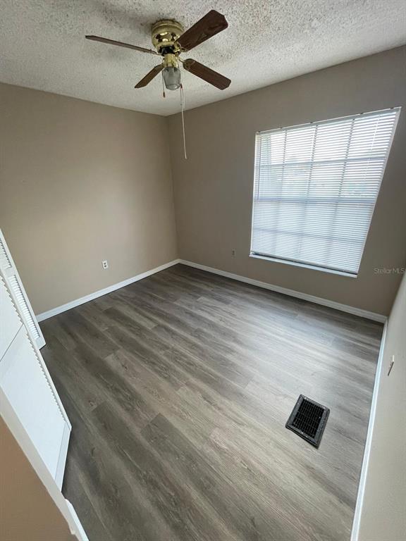 An empty bedroom features light-colored walls, wood-look flooring, a ceiling fan, and a window — 1300 ARLINGTON LANE NE UNIT 114, PALM BAY, FL