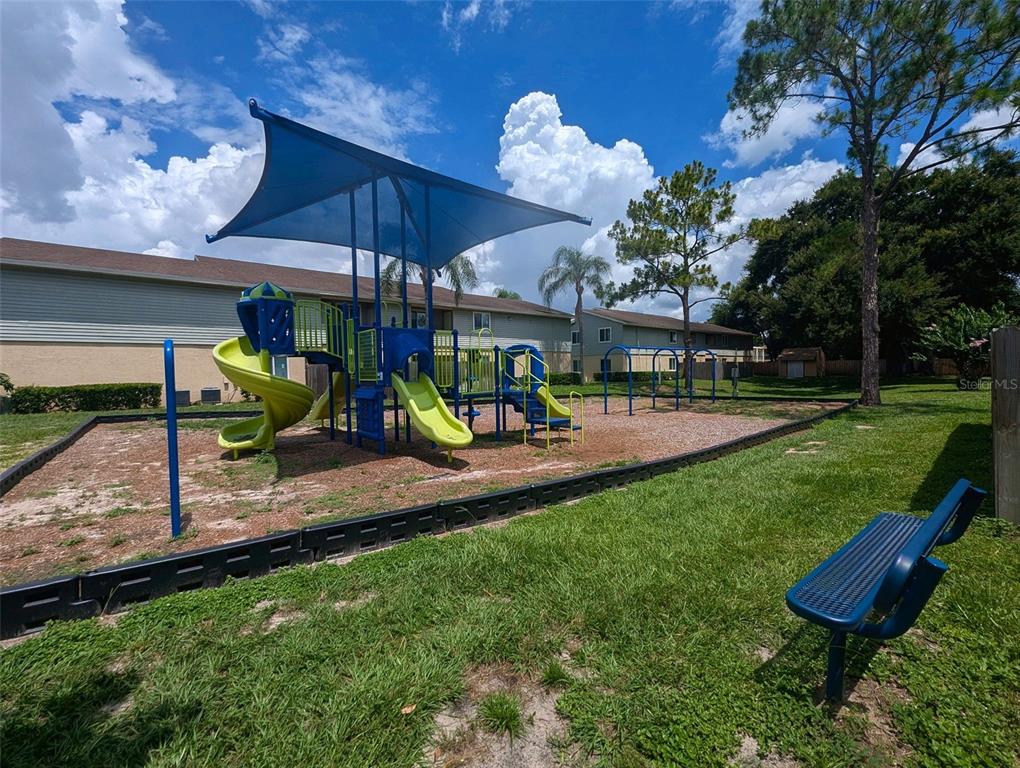 A playground with a blue shade structure, slides, and a bench on a grassy lot — 228 THORN TREE PLACE UNIT 228, BRANDON, FL