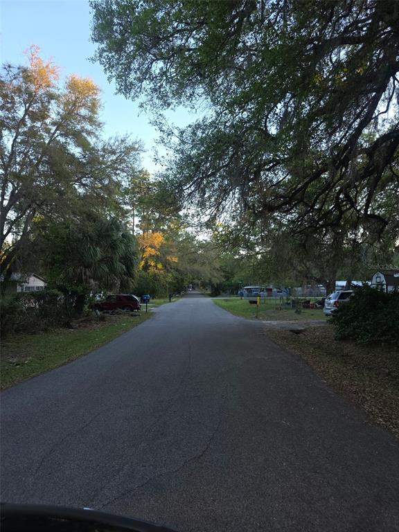 A paved residential street lined with mature trees and houses under a clear blue sky — 0 BETHUNE STREET, BROOKSVILLE, FL