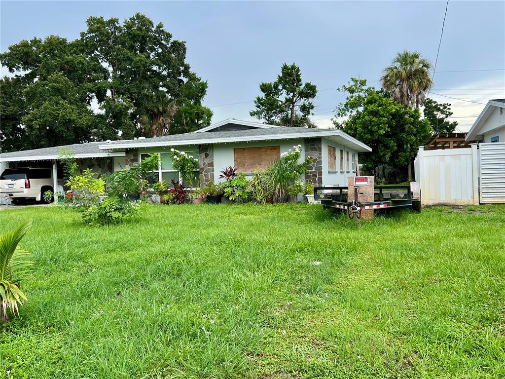A single-story house with a boarded-up window and a utility trailer parked on the lawn — 3246 EAGLE STREET, SARASOTA, FL
