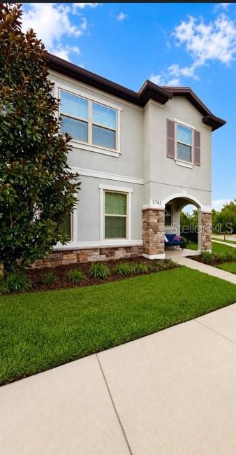 A two-story house exterior features light-colored stucco, stone accents, and a covered entryway — 5703 VILLAGE CENTER DRIVE, LITHIA, FL