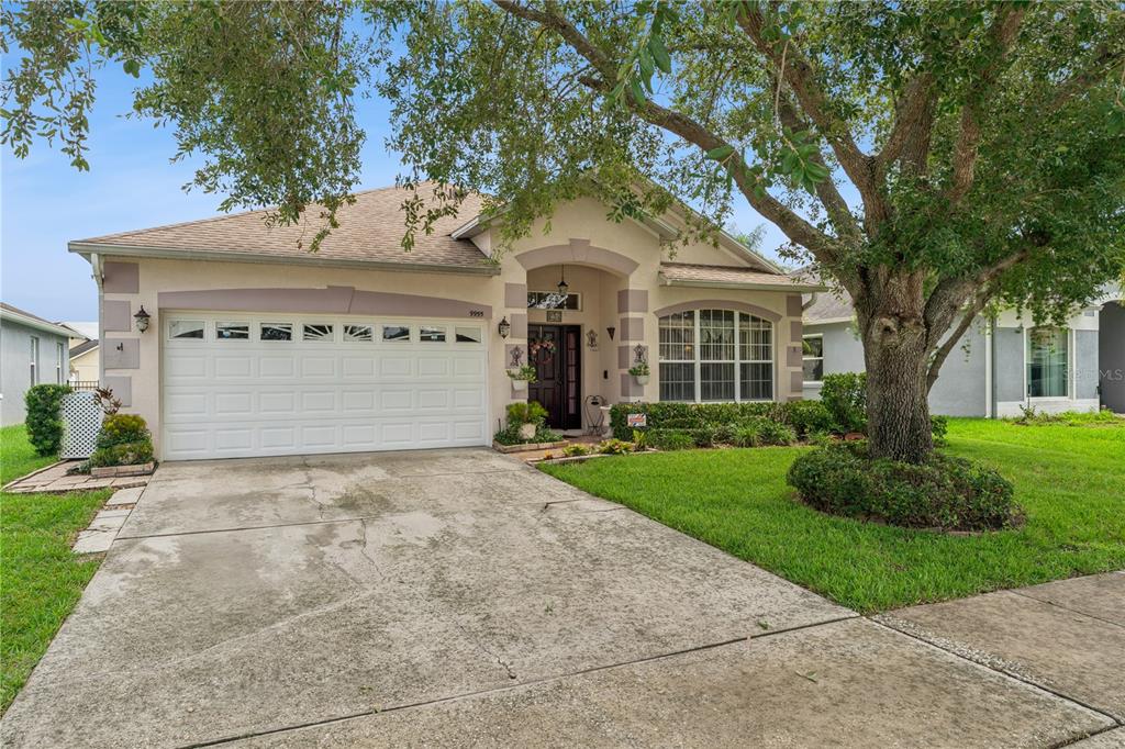 A single-story suburban house with a two-car garage, arched entryway, and a large front tree — 9955 MEDALLION BLUFF LANE, ORLANDO, FL