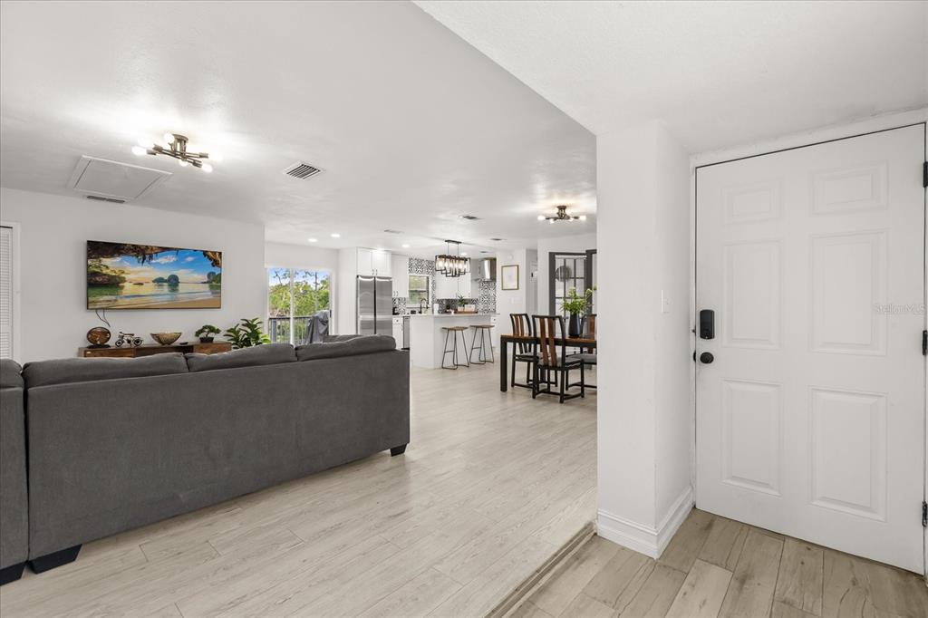 An open-concept living room and kitchen feature light wood flooring and a white front door — 5127 GLASGOW AVENUE, ORLANDO, FL