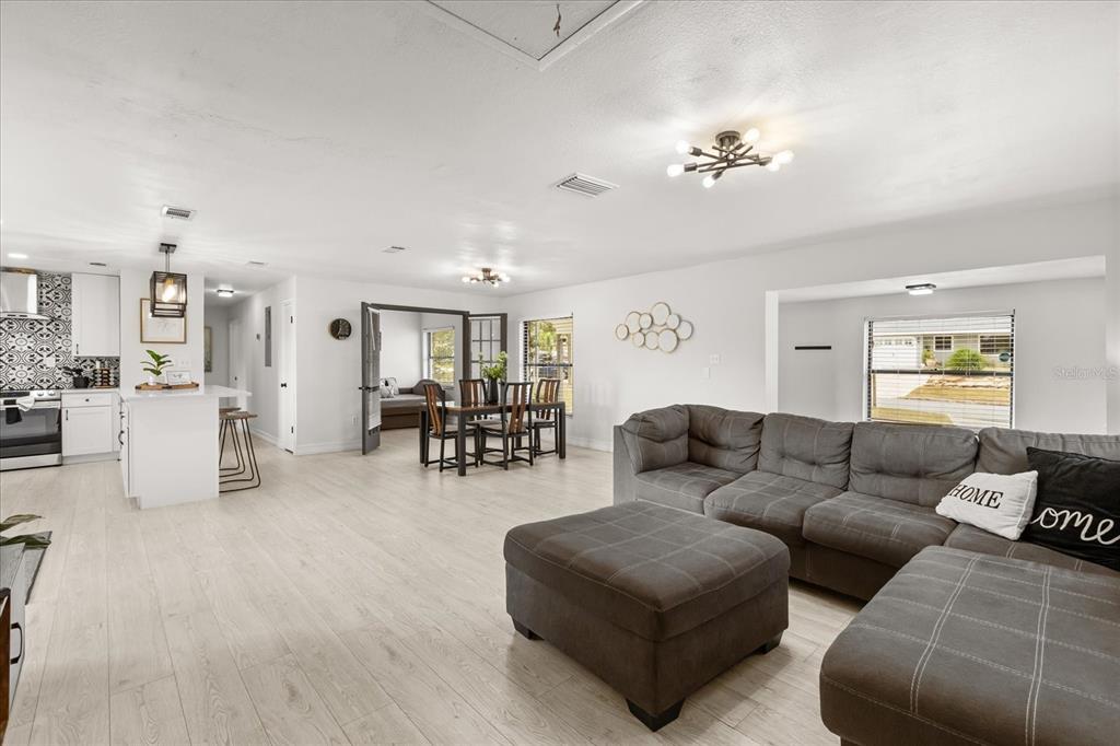 An open-concept living and dining area features light wood flooring, white walls, and gray furniture — 5127 GLASGOW AVENUE, ORLANDO, FL