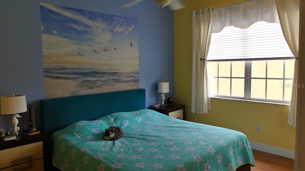 A bedroom features a teal headboard, a patterned bedspread, a beach mural, and yellow walls — 6801 DALI AVENUE UNIT 206, LAND O LAKES, FL