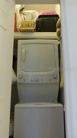 A stacked washer and dryer unit sits inside a closet with storage on the top shelf — 6801 DALI AVENUE UNIT 206, LAND O LAKES, FL