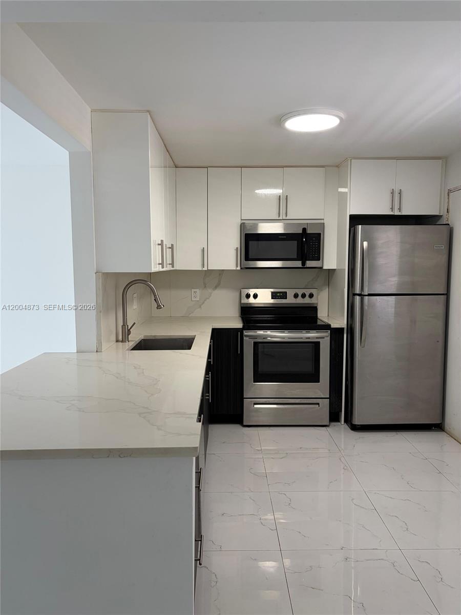 A modern kitchen features white cabinets, stainless steel appliances, and white marble-patterned countertops and flooring — 1401 NE 191st St # D201, Miami FL 33179, MIAMI, FL