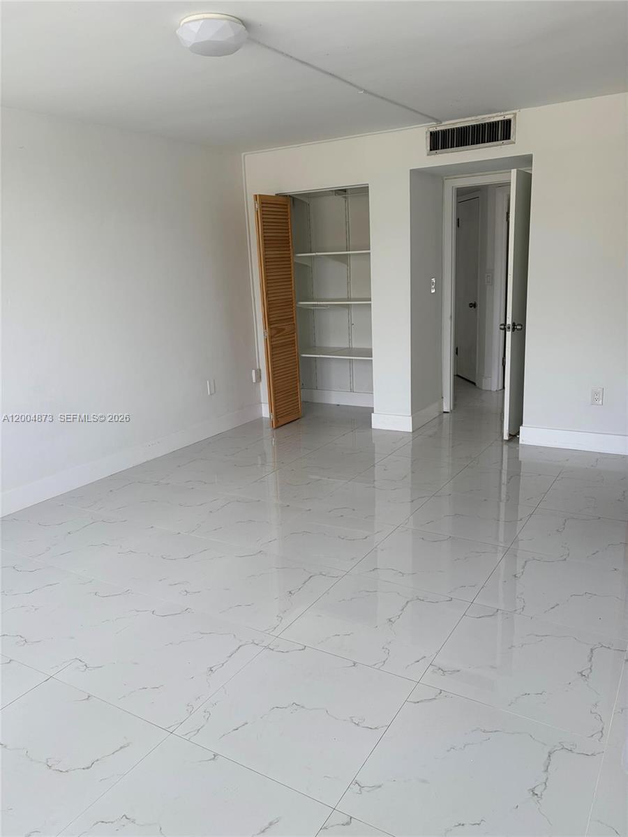 An empty room features white walls, white marble-patterned tile flooring, a built-in closet, and doorway — 1401 NE 191st St # D201, Miami FL 33179, MIAMI, FL