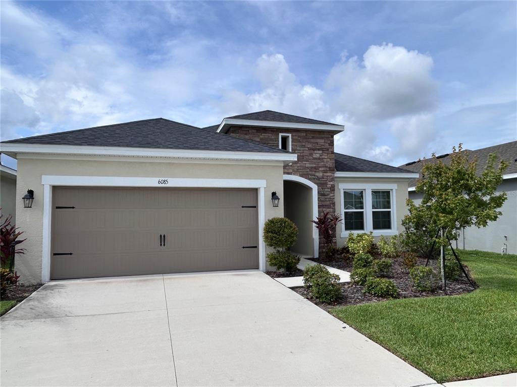 A single-story house features a tan stucco exterior, stone accents, and a two-car garage — 6085 HIDDEN BRANCH DRIVE, APOLLO BEACH, FL