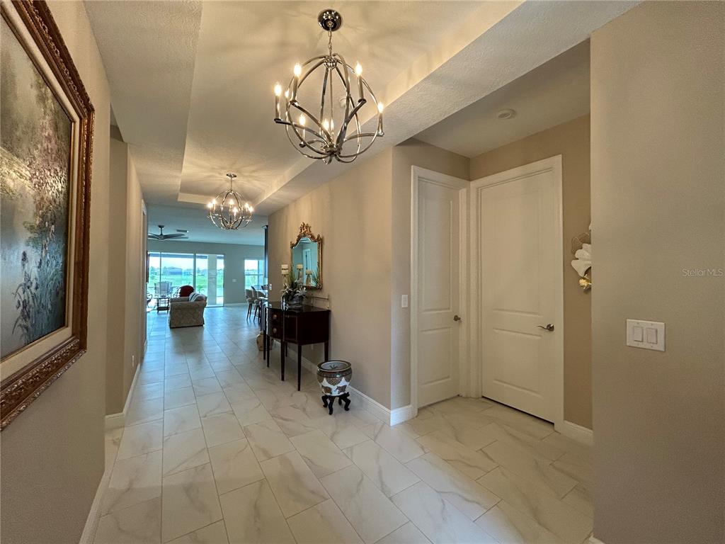 A tiled hallway leads to an open living area with two decorative chandeliers — 6085 HIDDEN BRANCH DRIVE, APOLLO BEACH, FL