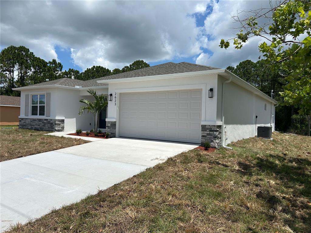 A single-story house with white stucco siding, a stone-accented base, and a side-entry garage — 2623 JUPITER BOULEVARD SW, PALM BAY, FL