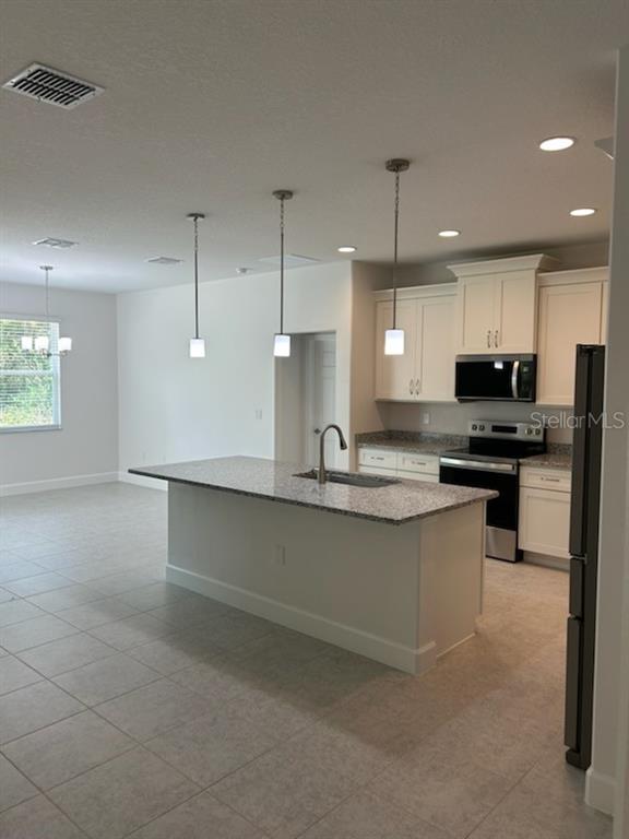 A kitchen features a granite-topped island, white cabinetry, stainless steel appliances, and tile flooring — 2623 JUPITER BOULEVARD SW, PALM BAY, FL
