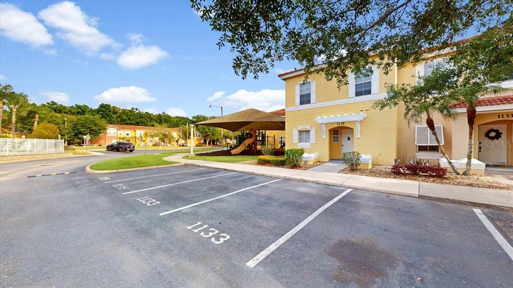 A paved parking lot sits in front of a yellow two-story building and a playground — 1135 PARK RIDGE CIRCLE, KISSIMMEE, FL