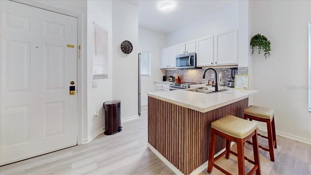 A kitchen features white cabinets, a wood-slatted island with bar stools, and light flooring — 1135 PARK RIDGE CIRCLE, KISSIMMEE, FL