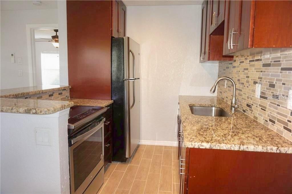 A galley kitchen features granite countertops, dark wood cabinets, stainless steel appliances, and tile flooring — 14026 E PARSLEY DRIVE, MADEIRA BEACH, FL
