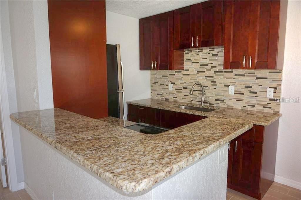 A kitchen features dark wood cabinets, granite countertops, and a multi-colored tile backsplash — 14026 E PARSLEY DRIVE, MADEIRA BEACH, FL
