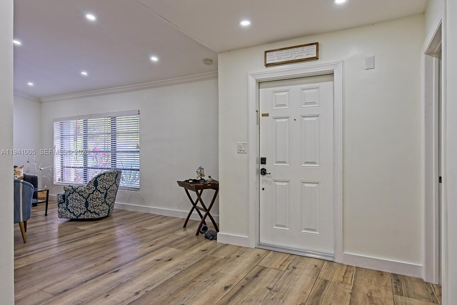 A bright entryway features wood-look flooring, a white front door, and a patterned armchair — 10900 SW 124th Rd, Miami FL 33176, MIAMI, FL