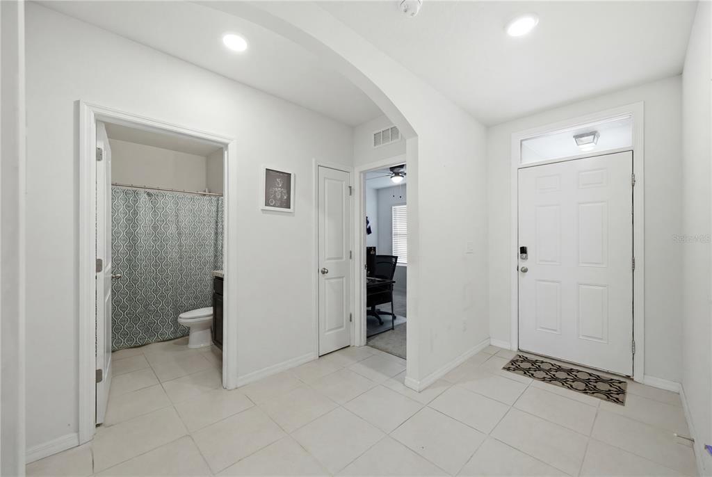 A bright entryway features white tile floors, an arched transition, a bathroom, and a front door — 36250 JENNY LYNNE DRIVE, ZEPHYRHILLS, FL