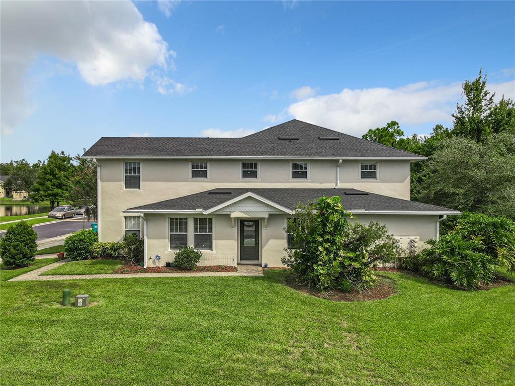 A two-story house with a light-colored stucco exterior, a dark shingled roof, and a front lawn — 5597 GELATO DRIVE, ORLANDO, FL