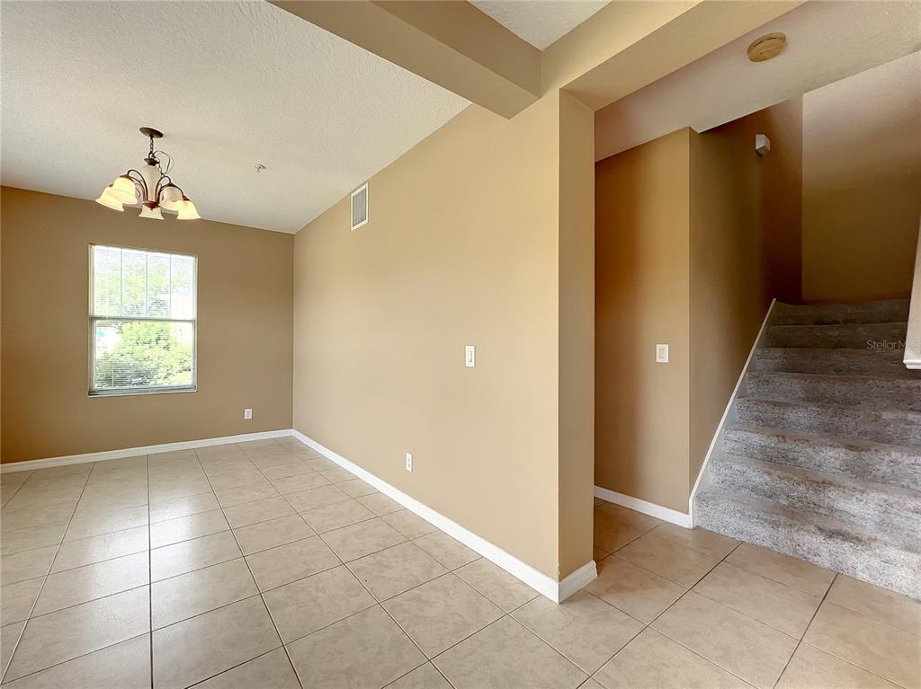 An interior view shows a tiled dining area with a chandelier next to carpeted stairs — 5597 GELATO DRIVE, ORLANDO, FL