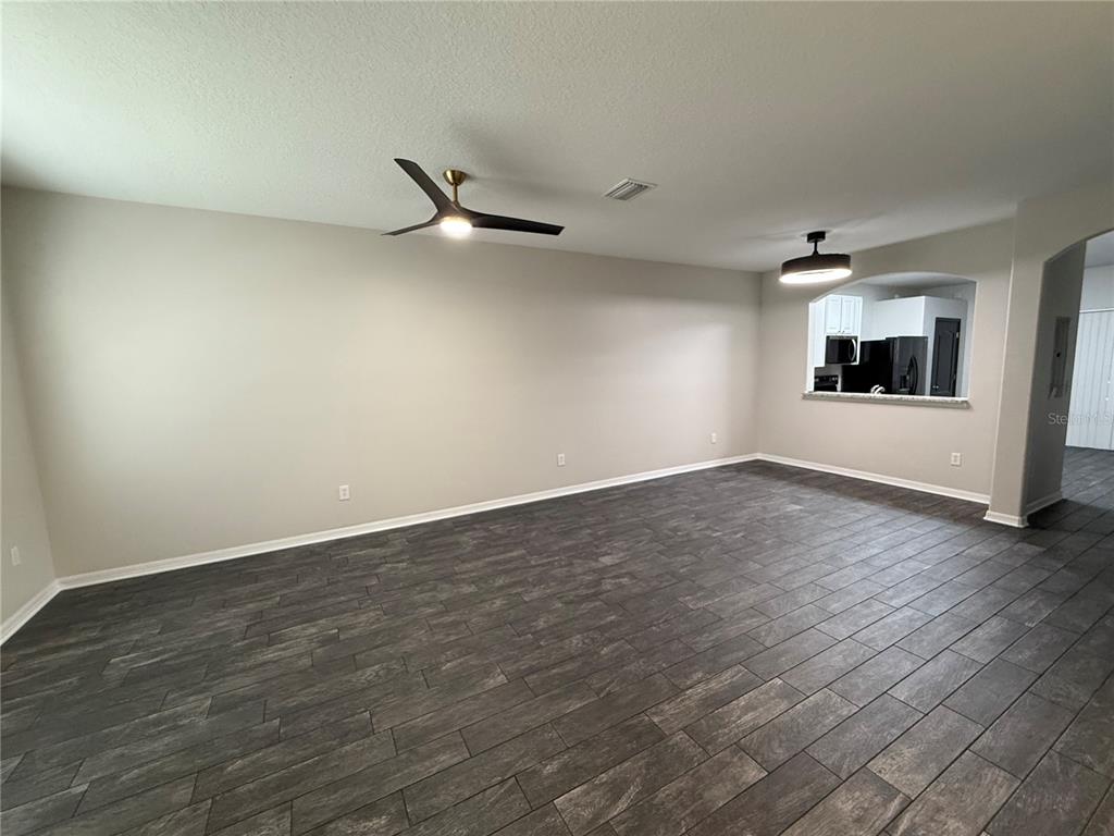 An empty room features dark wood-look tile flooring, a ceiling fan, and a kitchen pass-through — 30316 ELDERWOOD DRIVE, WESLEY CHAPEL, FL