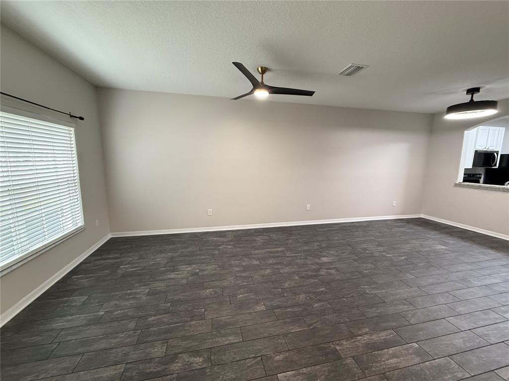 A spacious living room features light gray walls, dark wood-look tile flooring, and a ceiling fan — 30316 ELDERWOOD DRIVE, WESLEY CHAPEL, FL