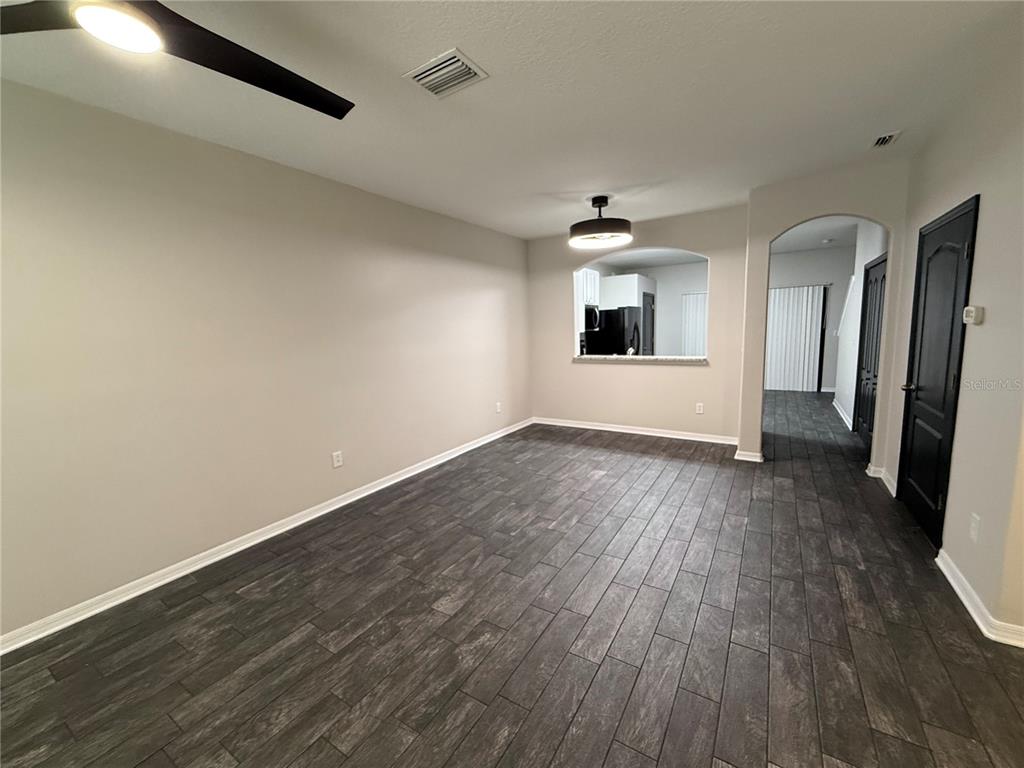 An empty room with dark wood-look tile flooring, light walls, and a kitchen pass-through window — 30316 ELDERWOOD DRIVE, WESLEY CHAPEL, FL