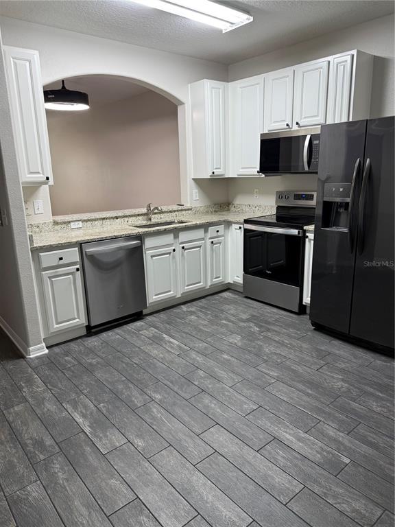 A kitchen features white cabinets, granite countertops, stainless steel appliances, and gray wood-look tile flooring — 30316 ELDERWOOD DRIVE, WESLEY CHAPEL, FL