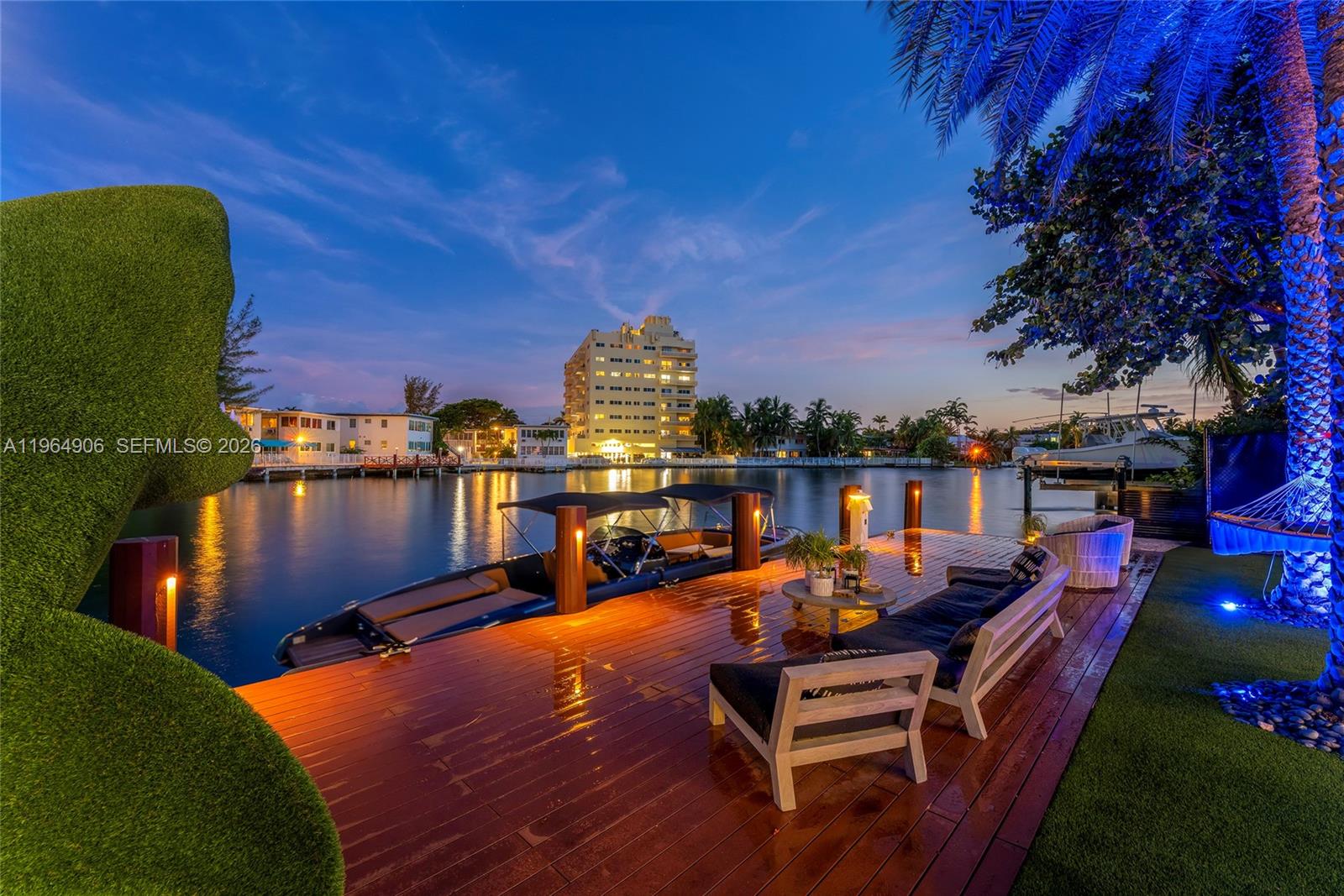 A wooden dock with outdoor seating overlooks a canal at sunset with a boat moored nearby — 528 Lakeview Ct, Miami Beach FL 33140, MIAMI BEACH, FL