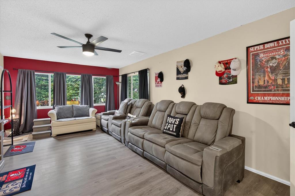 A living room features gray reclining theater seating, a white loveseat, and sports-themed wall decor — 10508 QUIMBY DRIVE, PORT RICHEY, FL