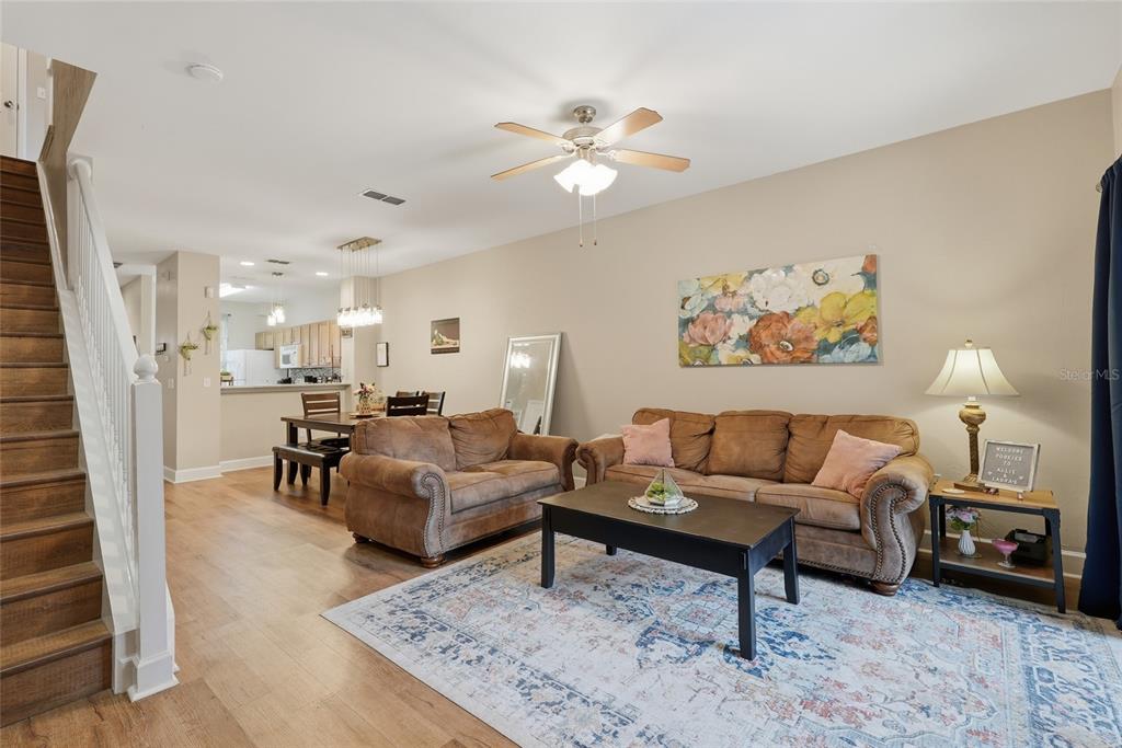 An open-concept living and dining area features wood-look flooring, a staircase, and neutral walls — 935 NW 21ST AVENUE UNIT 935, GAINESVILLE, FL