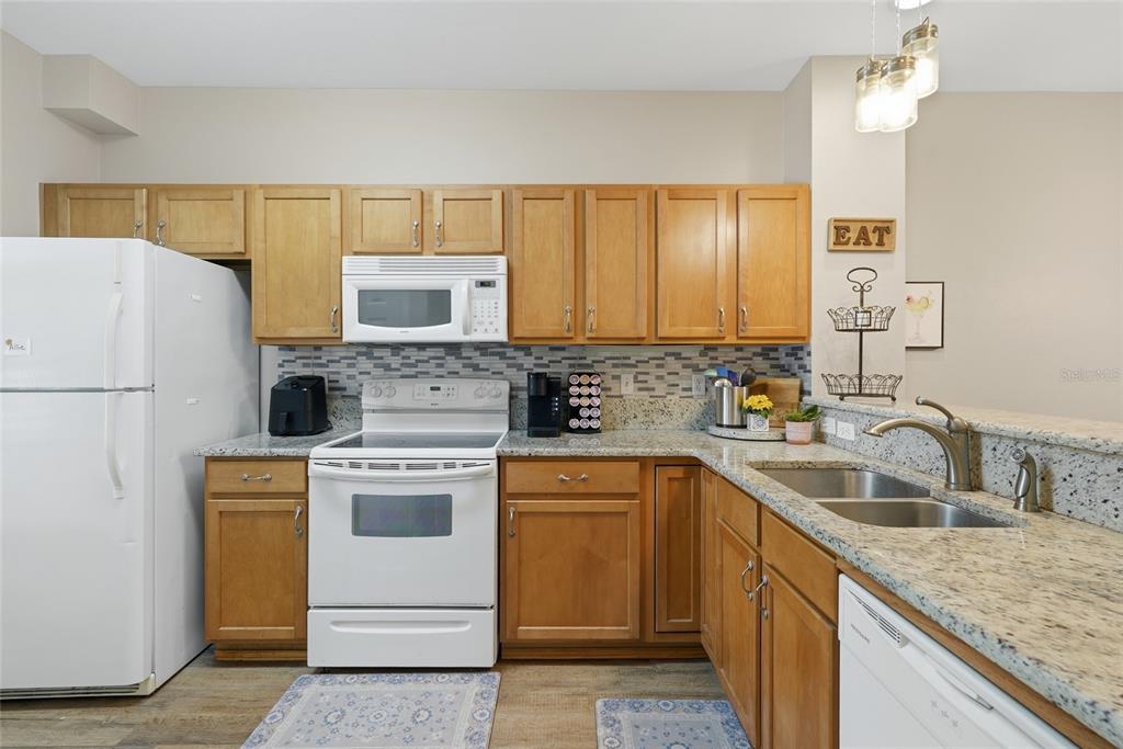 A kitchen features wood cabinets, granite countertops, white appliances, and a tiled backsplash — 935 NW 21ST AVENUE UNIT 935, GAINESVILLE, FL