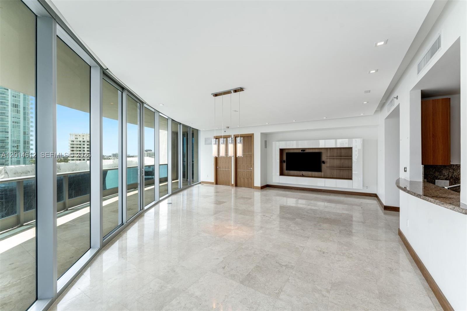 A spacious living room features marble floors, floor-to-ceiling windows, and a built-in media wall — 5959 Collins Ave # 1001, Miami Beach FL 33140, MIAMI BEACH, FL