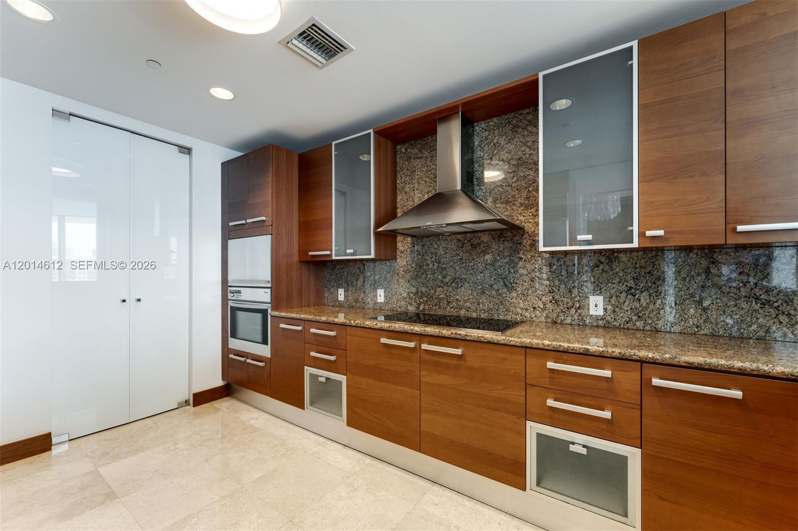A modern kitchen features wood cabinets, granite countertops, a stainless steel hood, and tile flooring — 5959 Collins Ave # 1001, Miami Beach FL 33140, MIAMI BEACH, FL