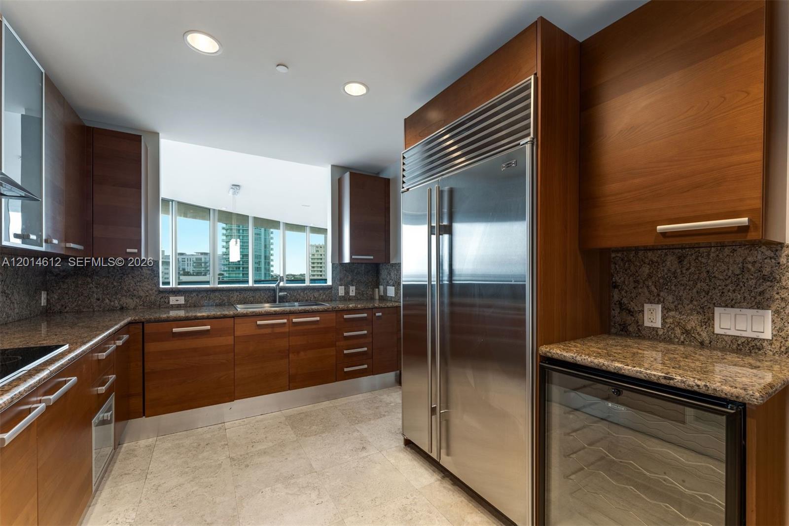 A modern kitchen features wood cabinets, granite countertops, stainless steel appliances, and a window view — 5959 Collins Ave # 1001, Miami Beach FL 33140, MIAMI BEACH, FL