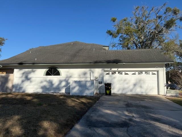 The exterior of a house features a white garage, a arched window, and a shingled roof — 450 LONGMEADOW LANE, LONGWOOD, FL