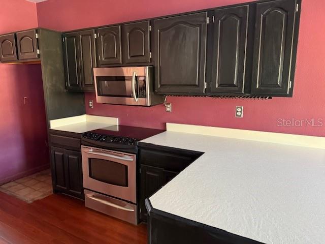 A kitchen features dark cabinets, stainless steel appliances, and white countertops against a magenta wall — 450 LONGMEADOW LANE, LONGWOOD, FL