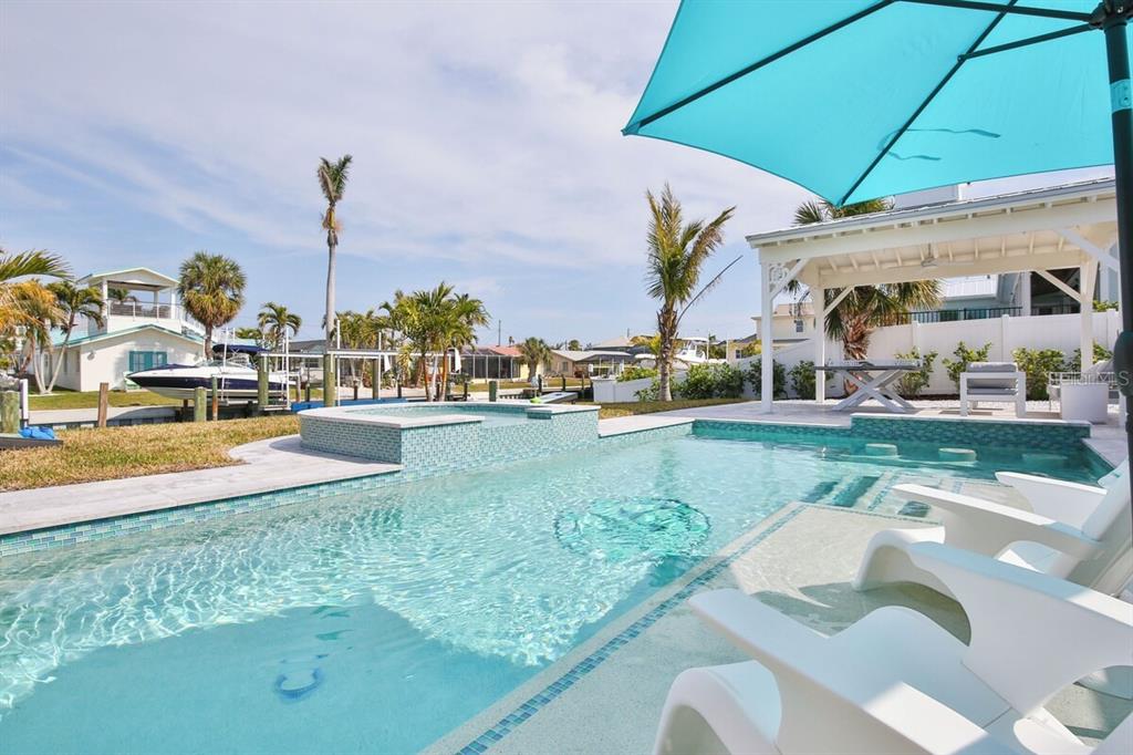 A swimming pool with a built-in spa and lounge chairs sits beside a covered patio — 605 CONCORD LANE, HOLMES BEACH, FL