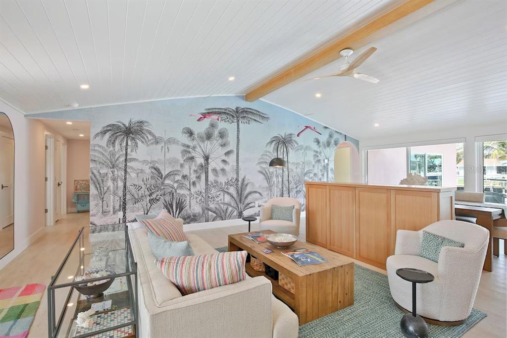 A living room features a palm tree mural, light wood furniture, and a vaulted ceiling — 605 CONCORD LANE, HOLMES BEACH, FL