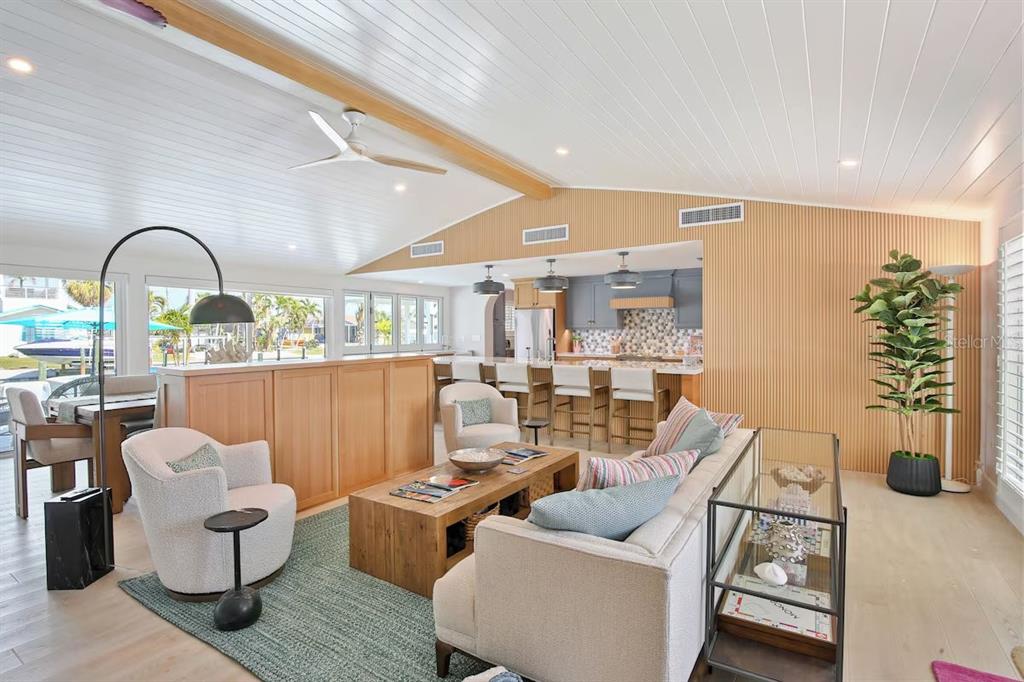 A bright open-concept living room features a vaulted ceiling, wood paneling, and a kitchen island — 605 CONCORD LANE, HOLMES BEACH, FL