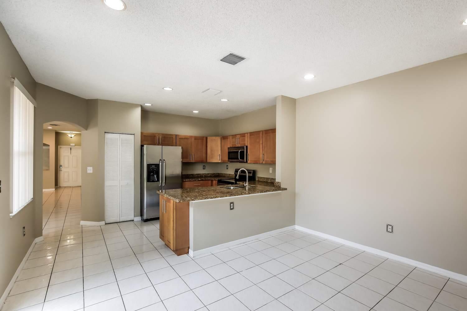 A kitchen features wood cabinets, granite countertops, stainless steel appliances, and white tile flooring — COOPER CITY, FL
